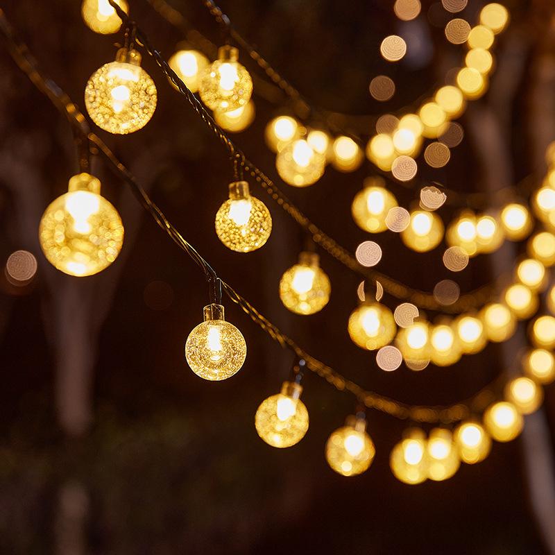 Warm white solar globe string lights strung in a backyard tree at dusk
